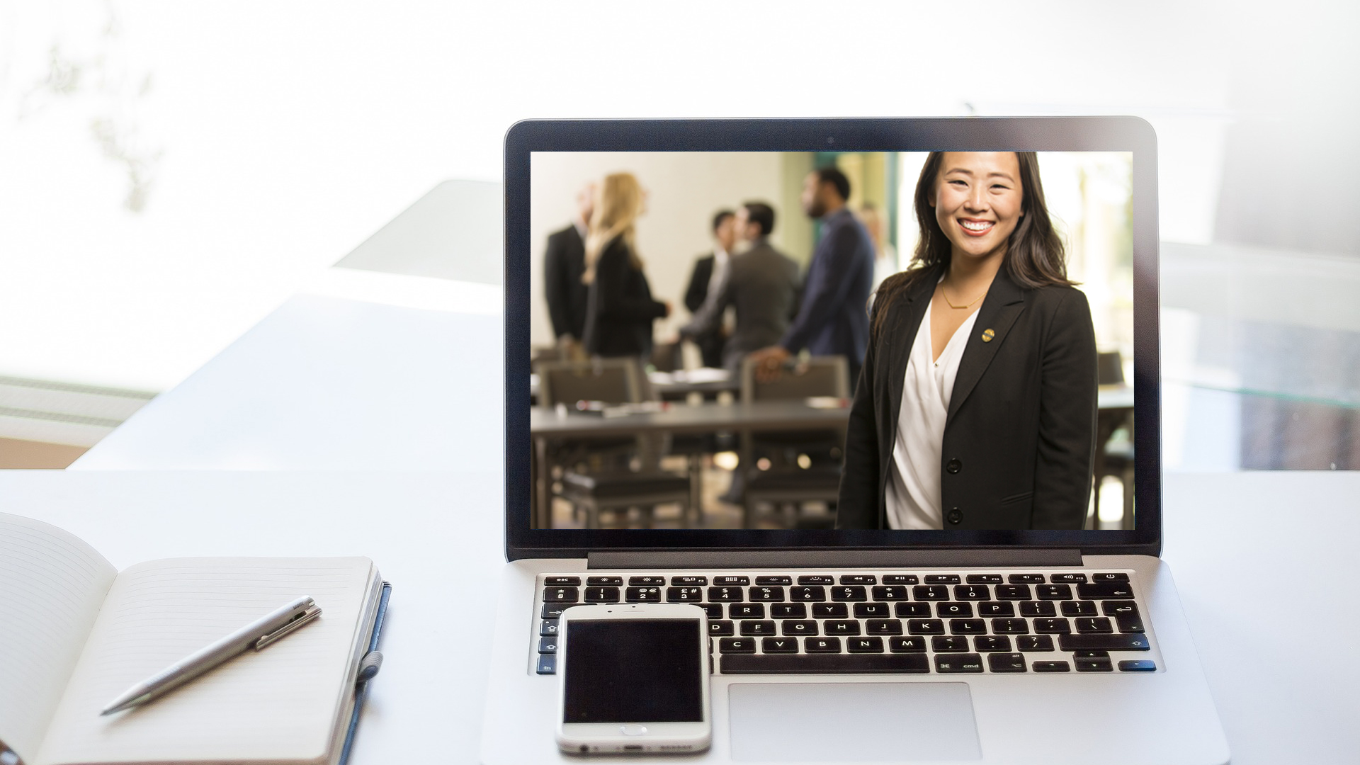 Laptop with a women smiling on the screen and people blurred behind her.